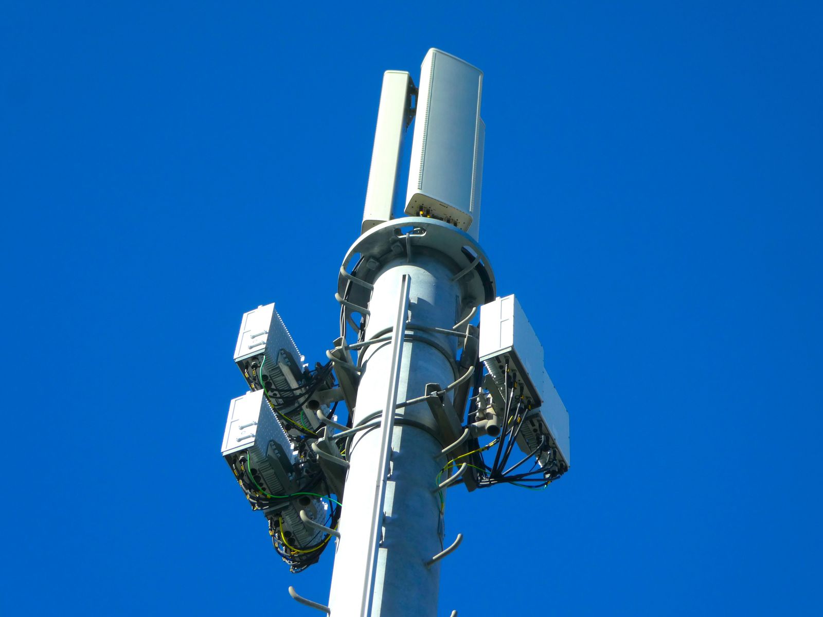 Moderner Mobilfunkmast mit Antennentechnik vor strahlend blauem Himmel